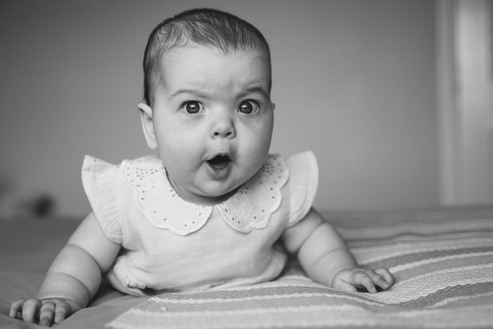 Black and white portrait of wide-eyed baby in white dress.
