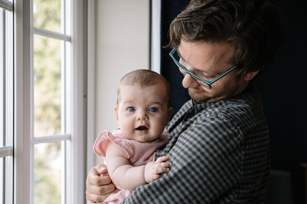 A heartwarming window-lit moment between a parent and baby wearing pink.