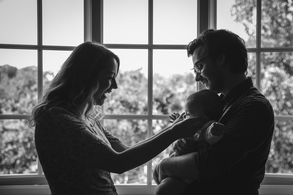 A tender family moment silhouetted by window light as parents share quiet time with their newborn.