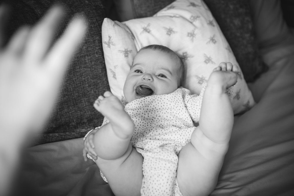 A laughing baby lying on a pillow reaching up toward the camera.