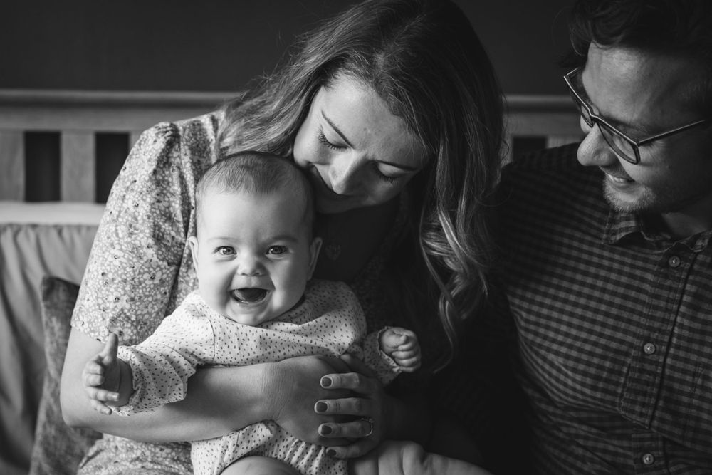 A black and white capture of a happy family moment with their smiling infant.