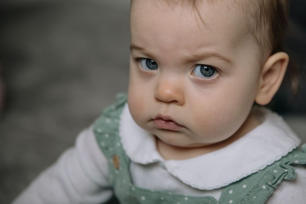 Close up of a baby with striking blue eyes wearing a green dress with white collar.