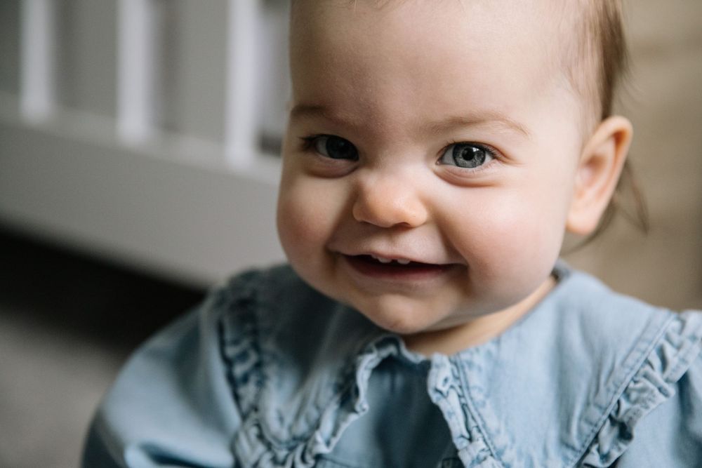 Close up portrait of a smiling baby with bright blue eyes wearing a blue collared outfit.