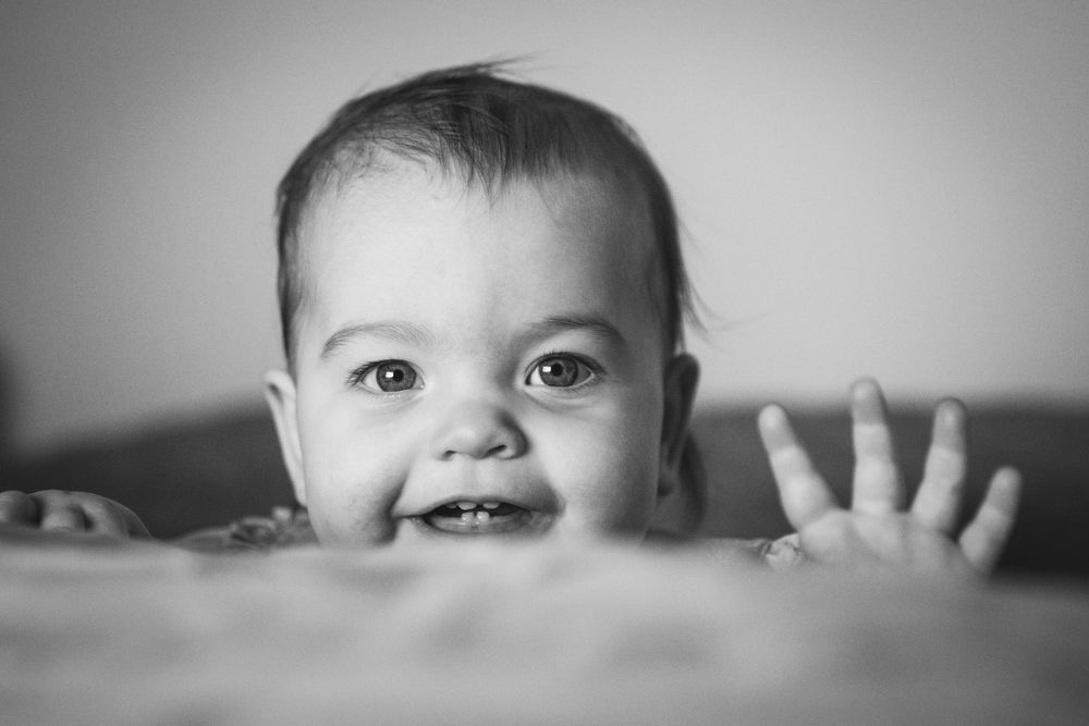 A close-up black and white portrait of a smiling baby peeking over an edge.