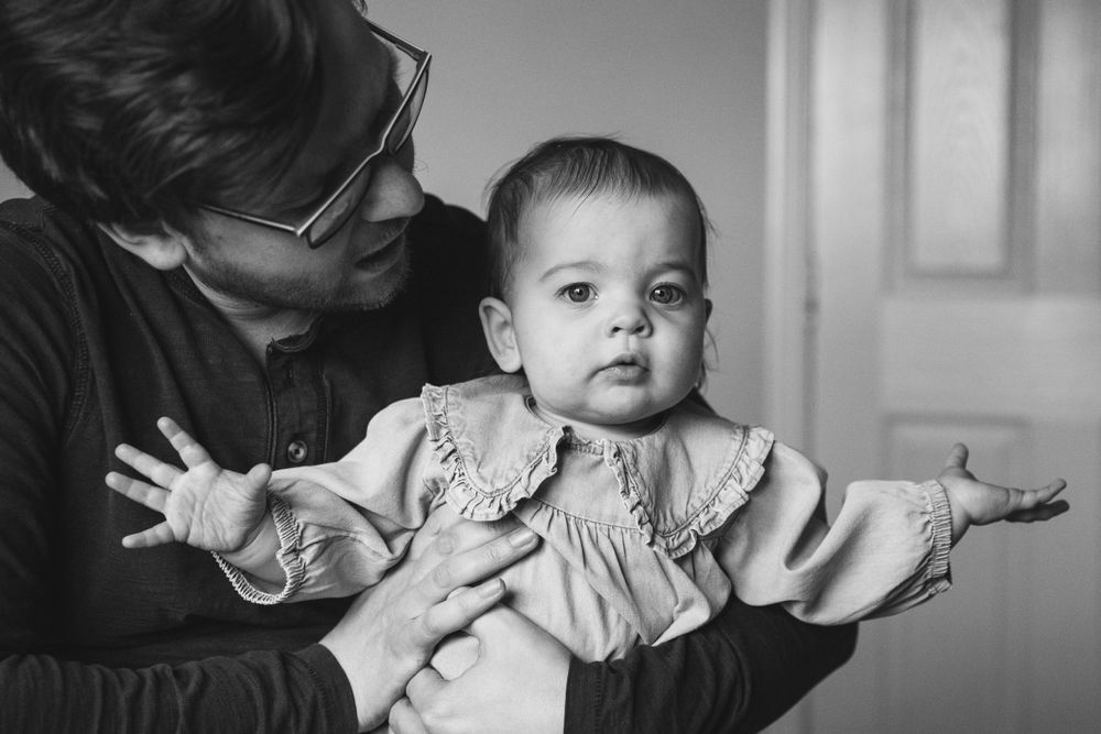 A black and white portrait of a baby with outstretched arms.