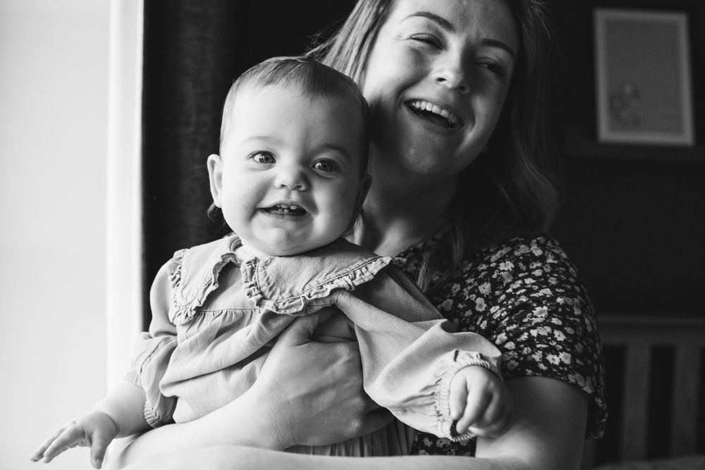 A tender black and white moment between a baby in a light dress and caregiver smiling together.
