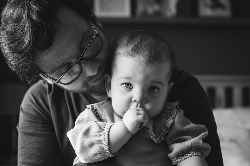 Black and white portrait of a baby sucking thumb while being held by caregiver.