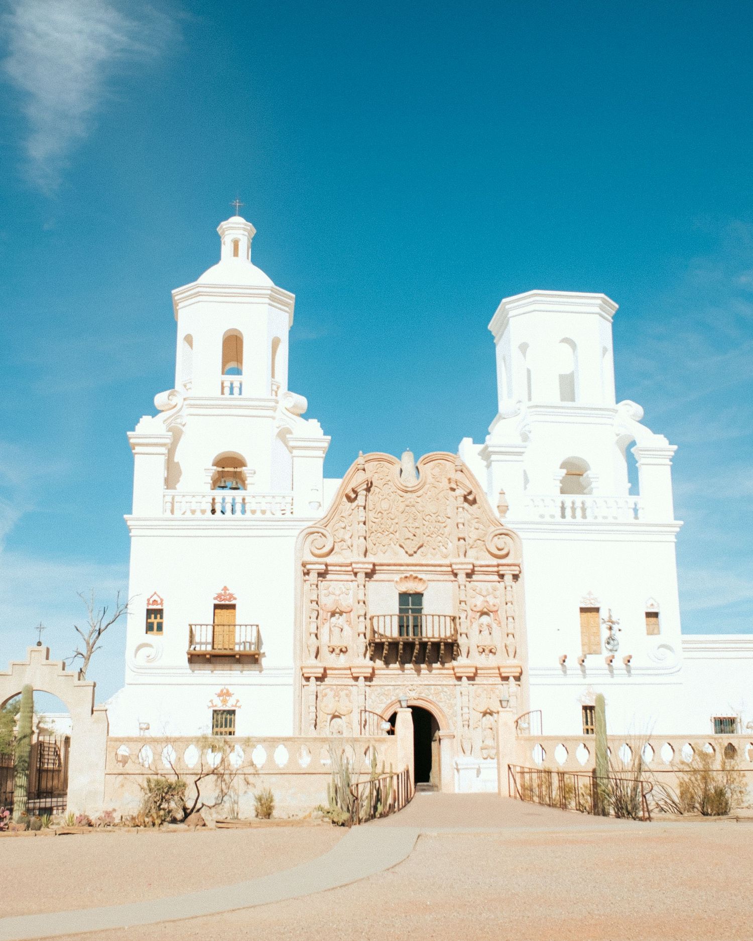 White Spanish colonial mission church with twin bell towers against bright blue sky.