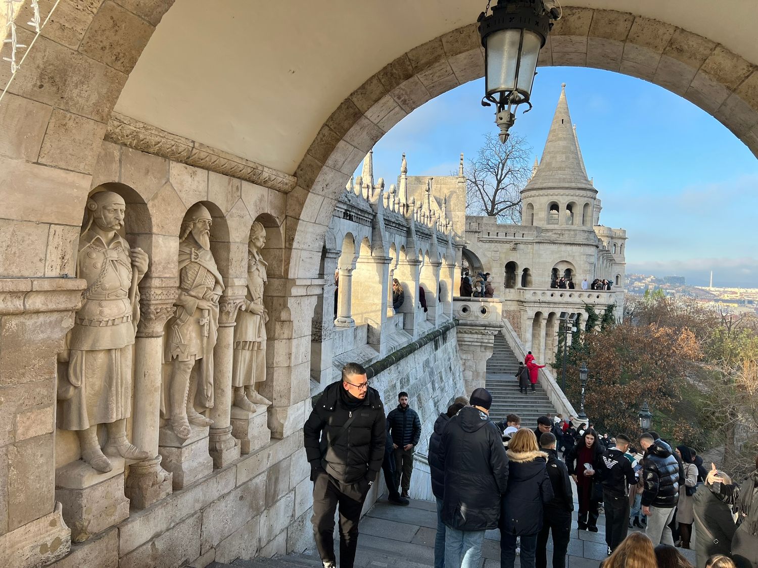 Tourists walk along the ornate stone arched gallery of Fishermans Bastion in Budapest on a clear winter day.