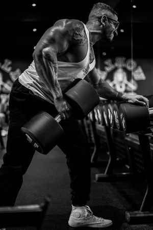 Muscular man doing dumbbell rows in gym, black and white fitness photo.