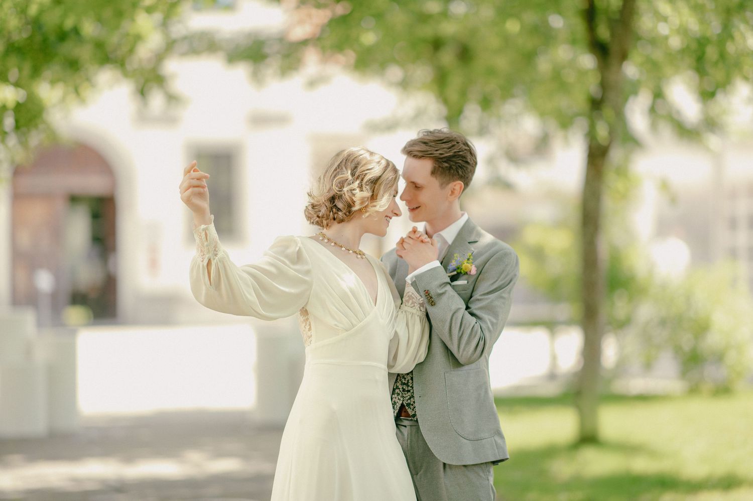 Bride and groom sharing a romantic moment outdoors, with the bride raising her hand while the groom kisses it.