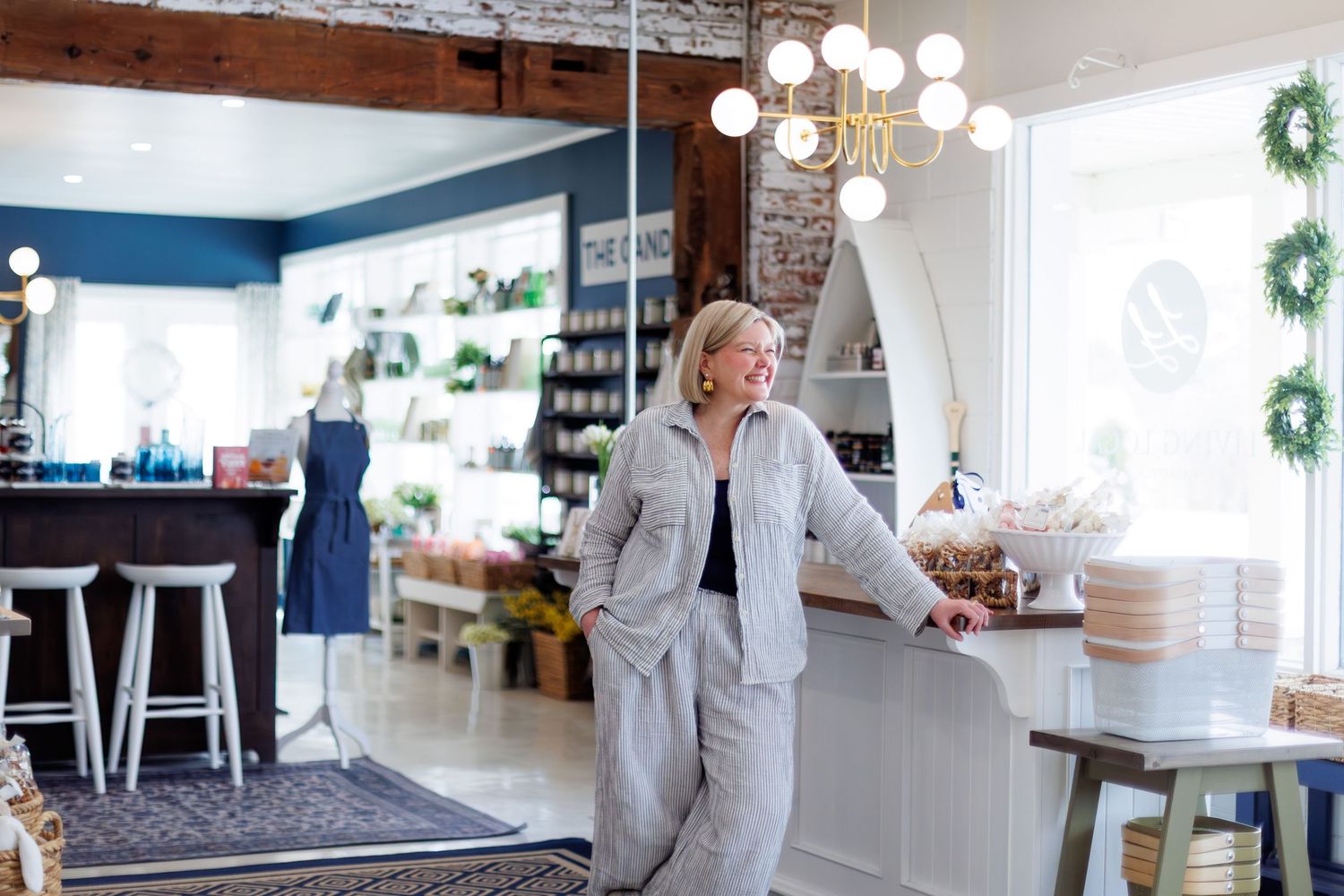 Woman leaning on a counter in a charming boutique shop with blue walls and elegant chandelier lighting.