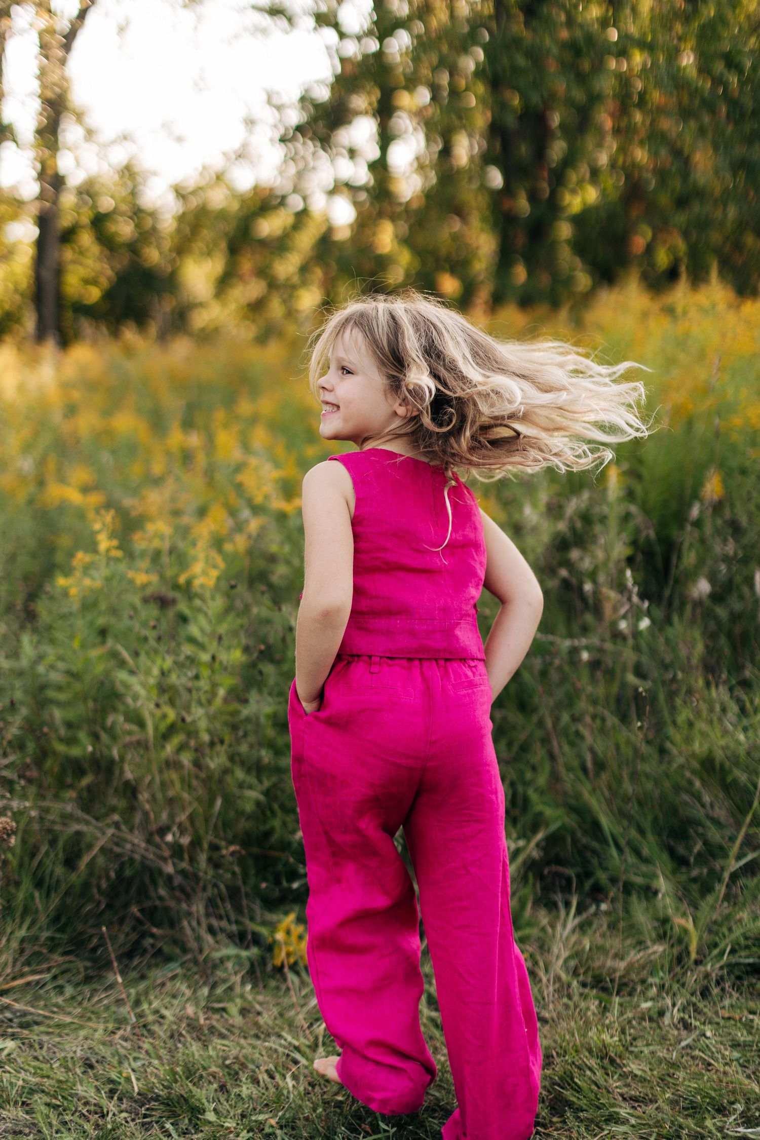 Young girl in pink jumpsuit twirling in a sunlit wildflower meadow at sunset.
