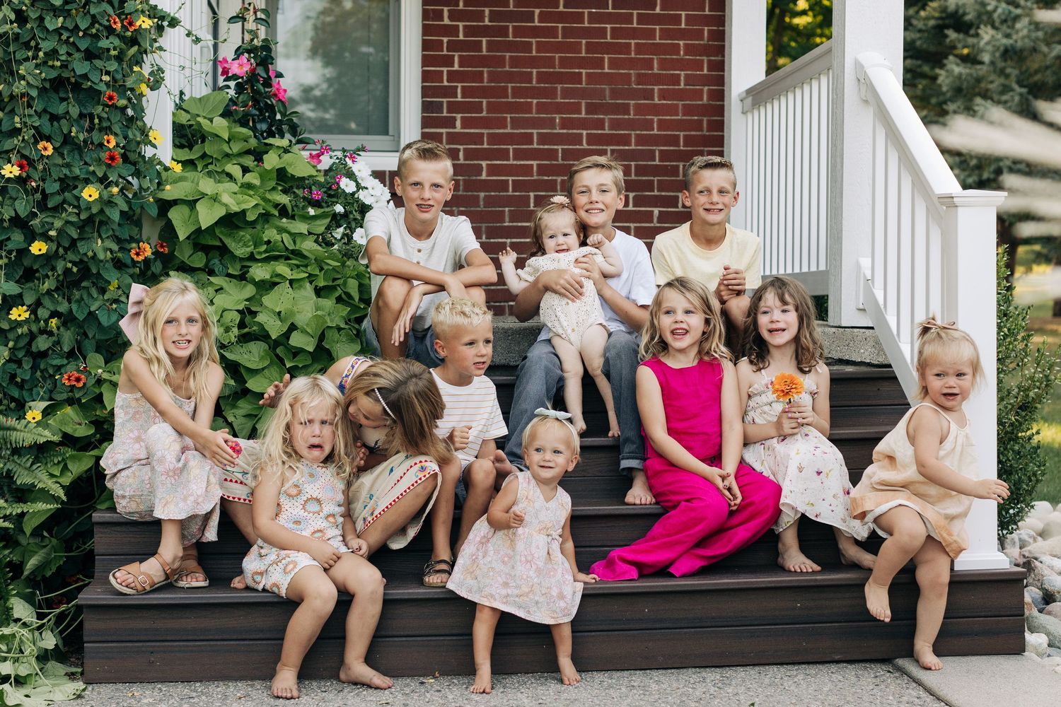 Group of children sitting on front porch steps smiling together outside brick home.