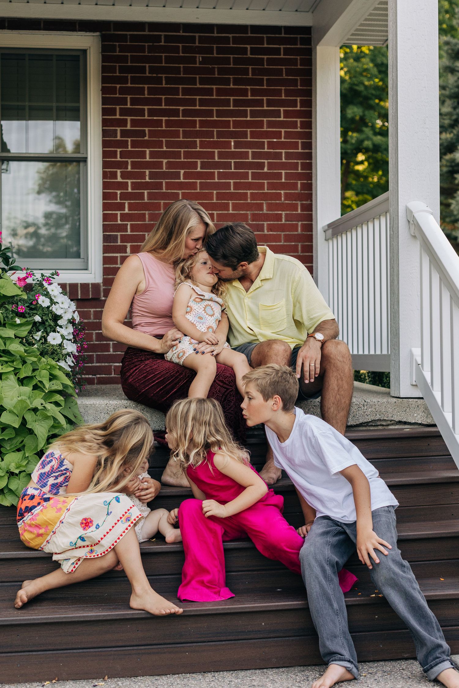 Family of five sharing a tender moment together on brick home front porch steps.