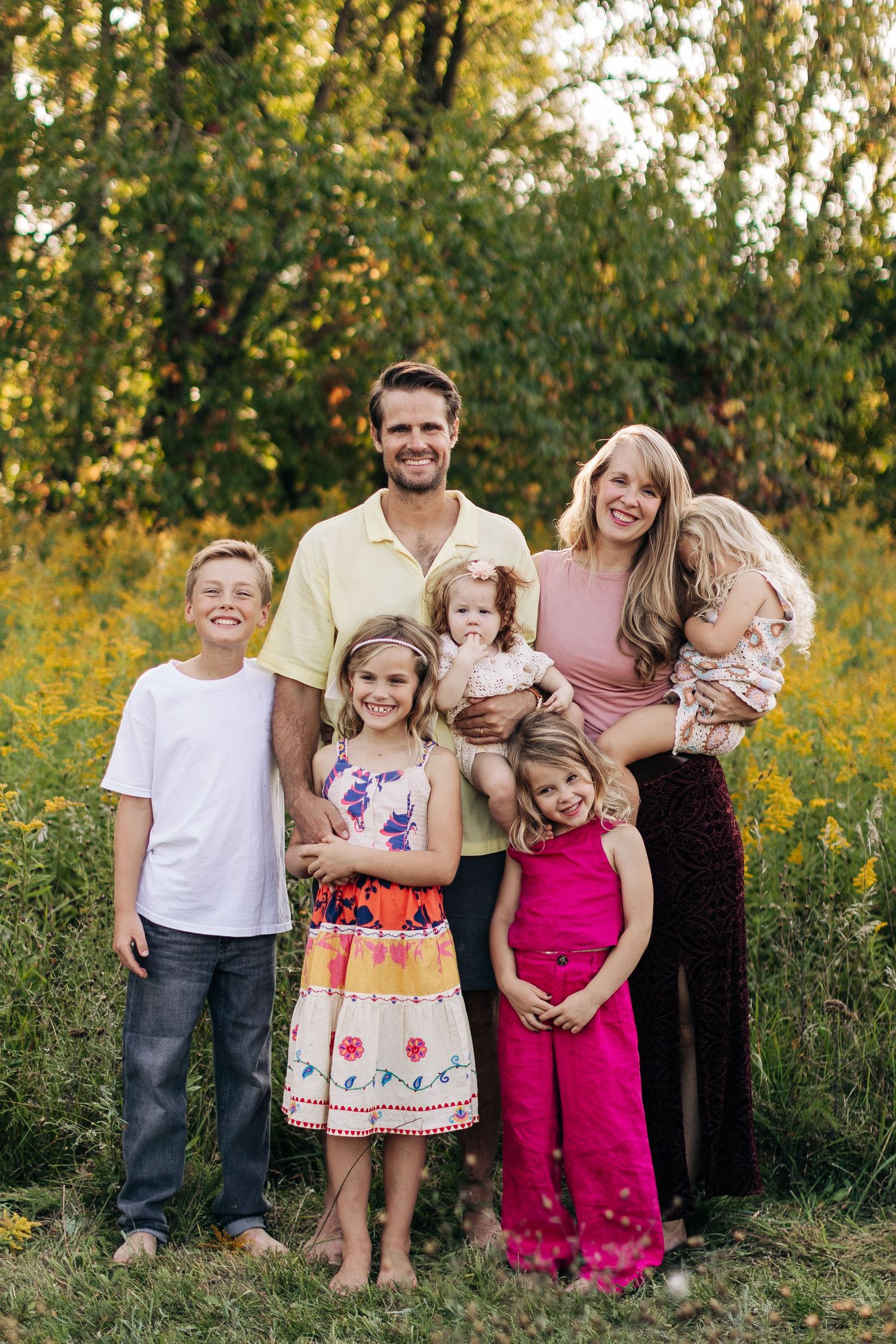 Happy family of six posing together in a golden wildflower field during sunset.