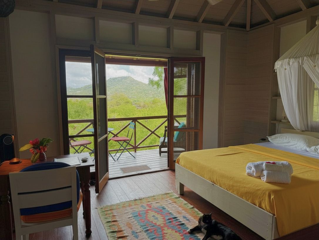 Cozy tropical bungalow bedroom with yellow bedding, canopy bed, and open balcony doors revealing lush mountain views.