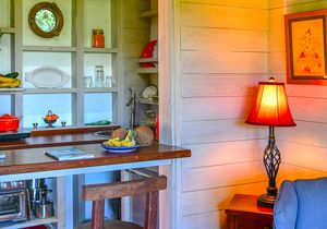 Cozy tiny home interior with wooden bar counter, red lamp, built-in shelves, and warm rustic decor.