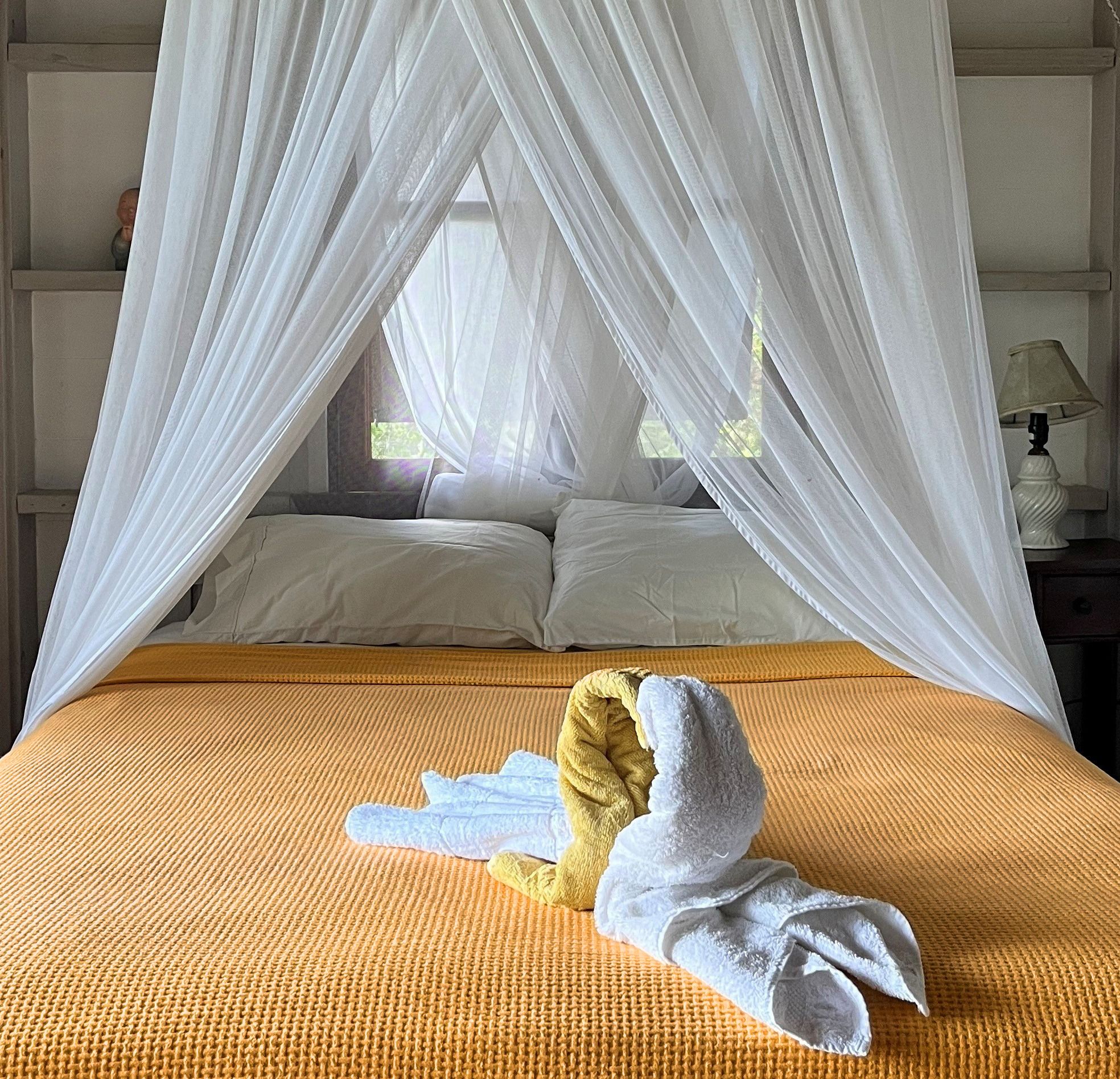 Elegant canopy bed with white drapes and yellow bedspread, adorned with decorative towel animals on top.