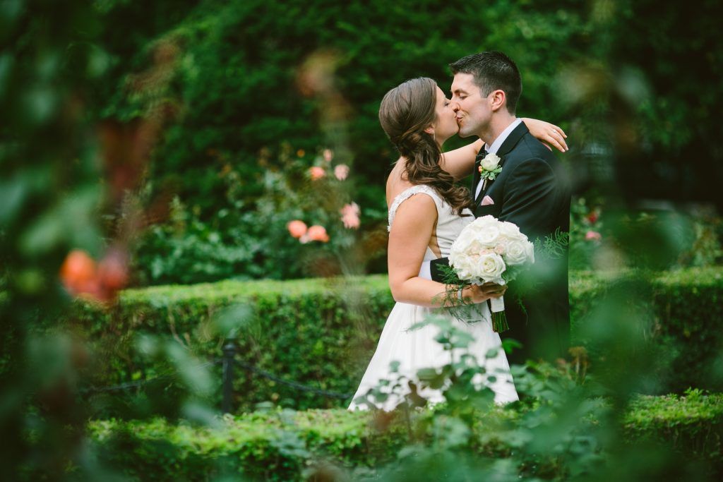 Romantic wedding couple kissing in garden with white bouquet.