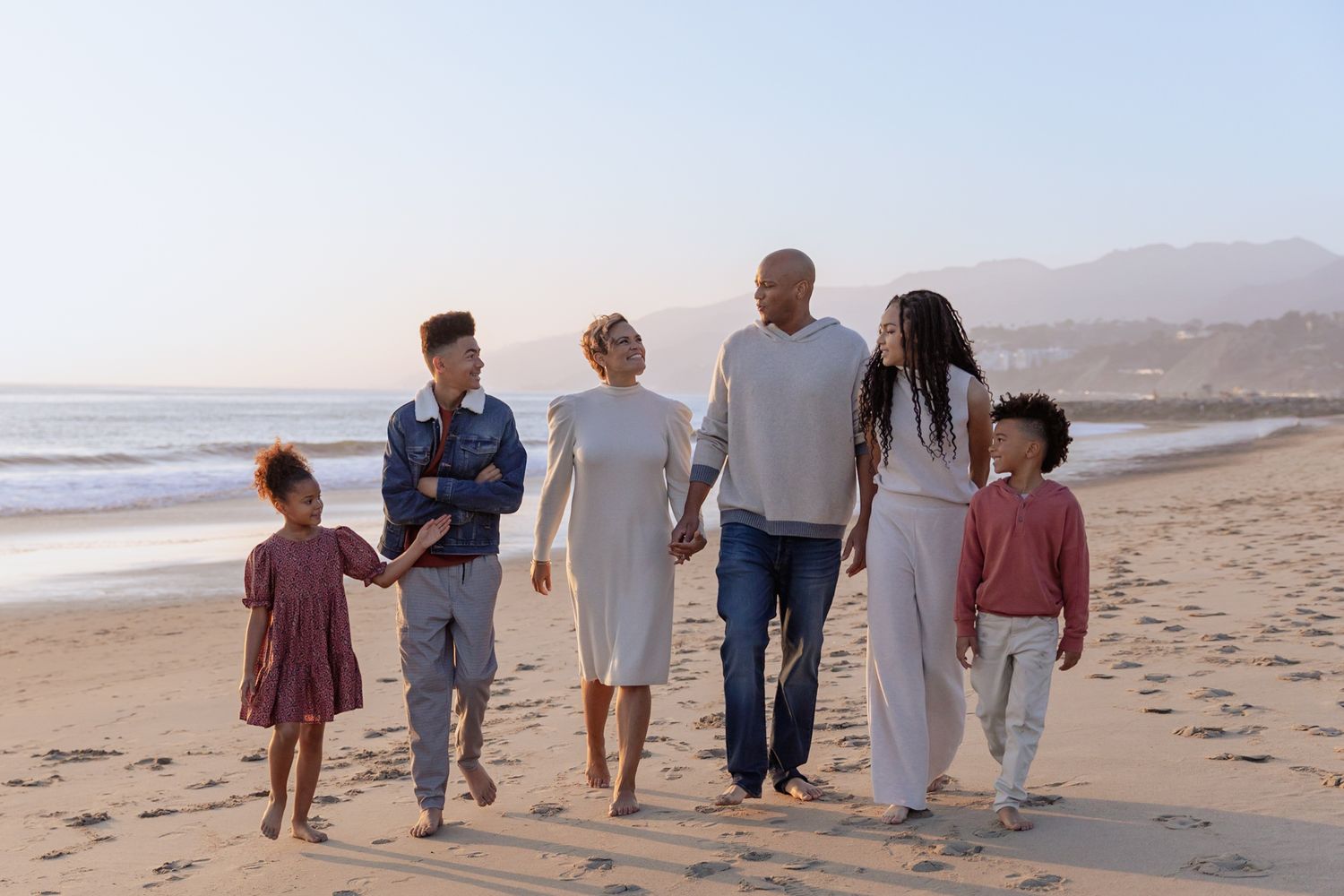 Happy multigenerational family of six walking together on a sunny beach at sunset.