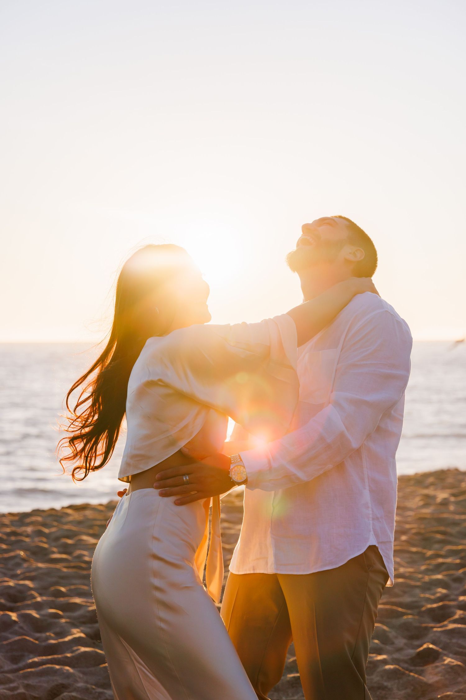 Romantic couple embracing on the beach with golden sunset light and ocean in the background.