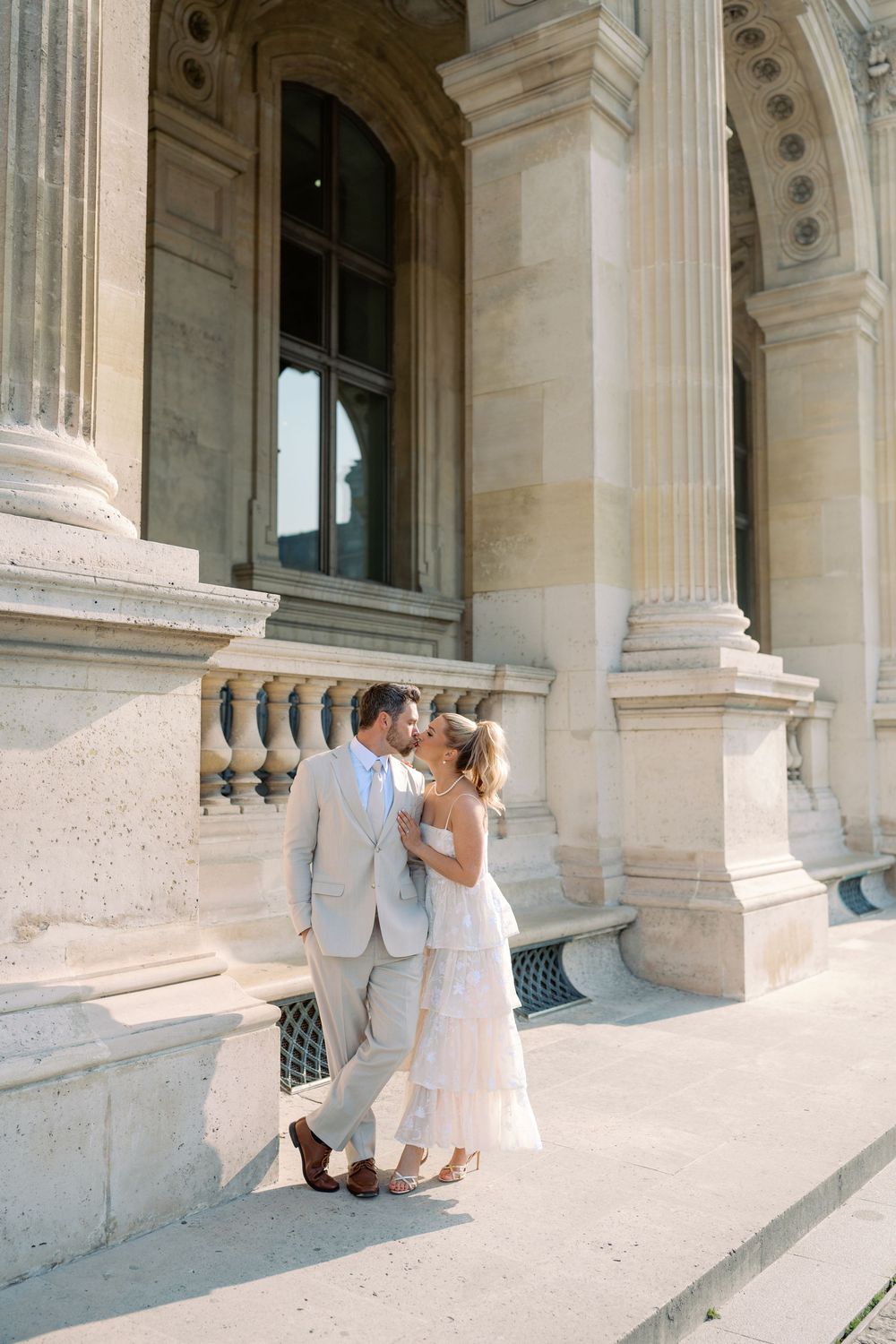 Couple sharing a romantic kiss in front of a grand classical stone building with ornate columns in Paris.