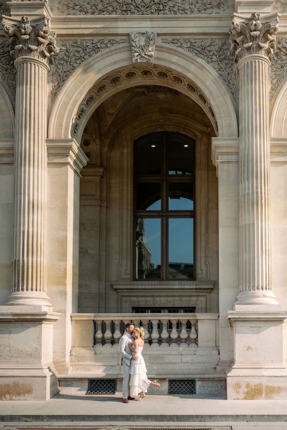 Bride and groom embracing under an ornate arched doorway of a historic Parisian building.