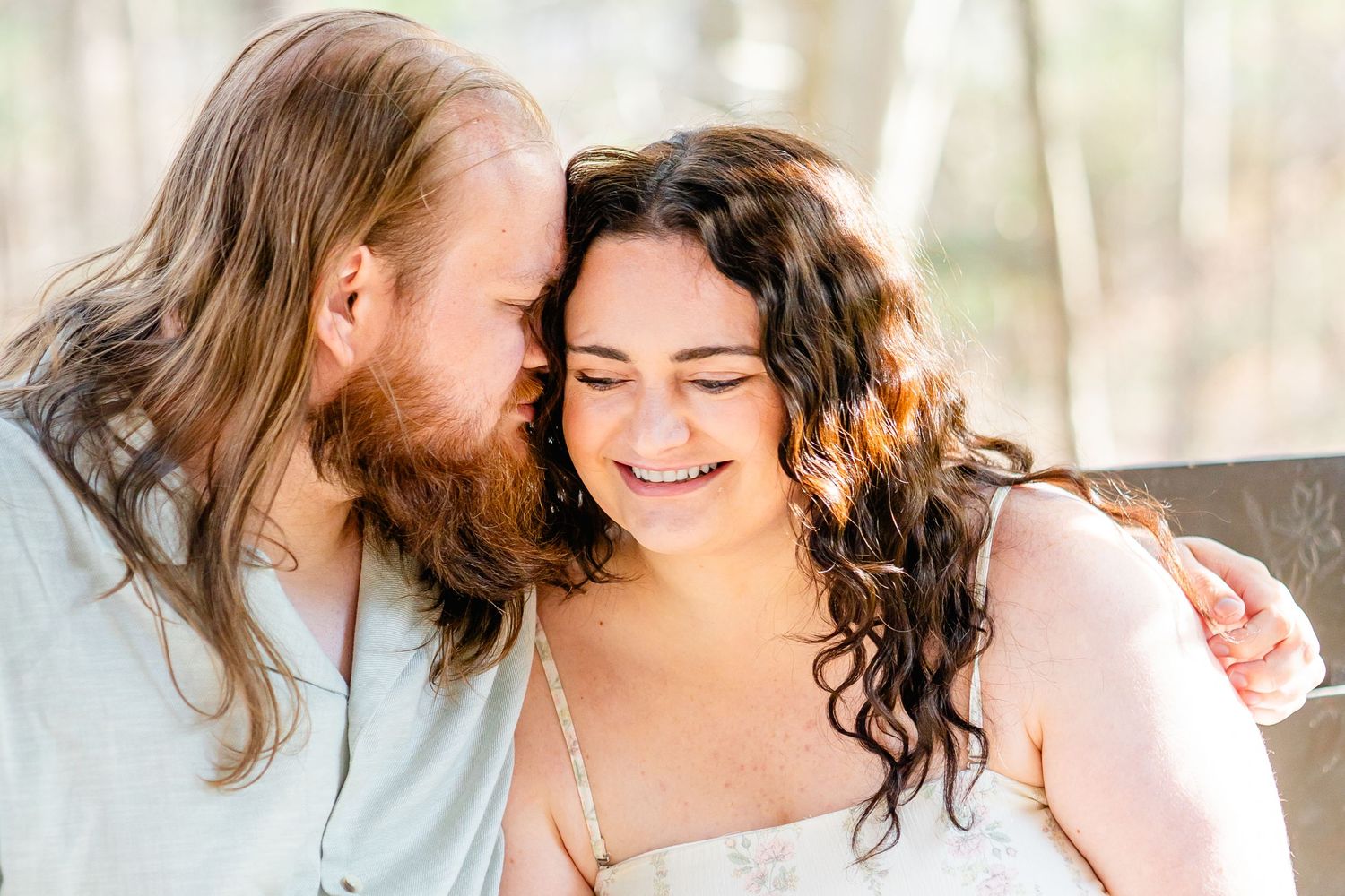 a man whispering to a smiling curly-haired woman in a romantic outdoor setting. engagement sunset morgantown wv botanical gardens spring
