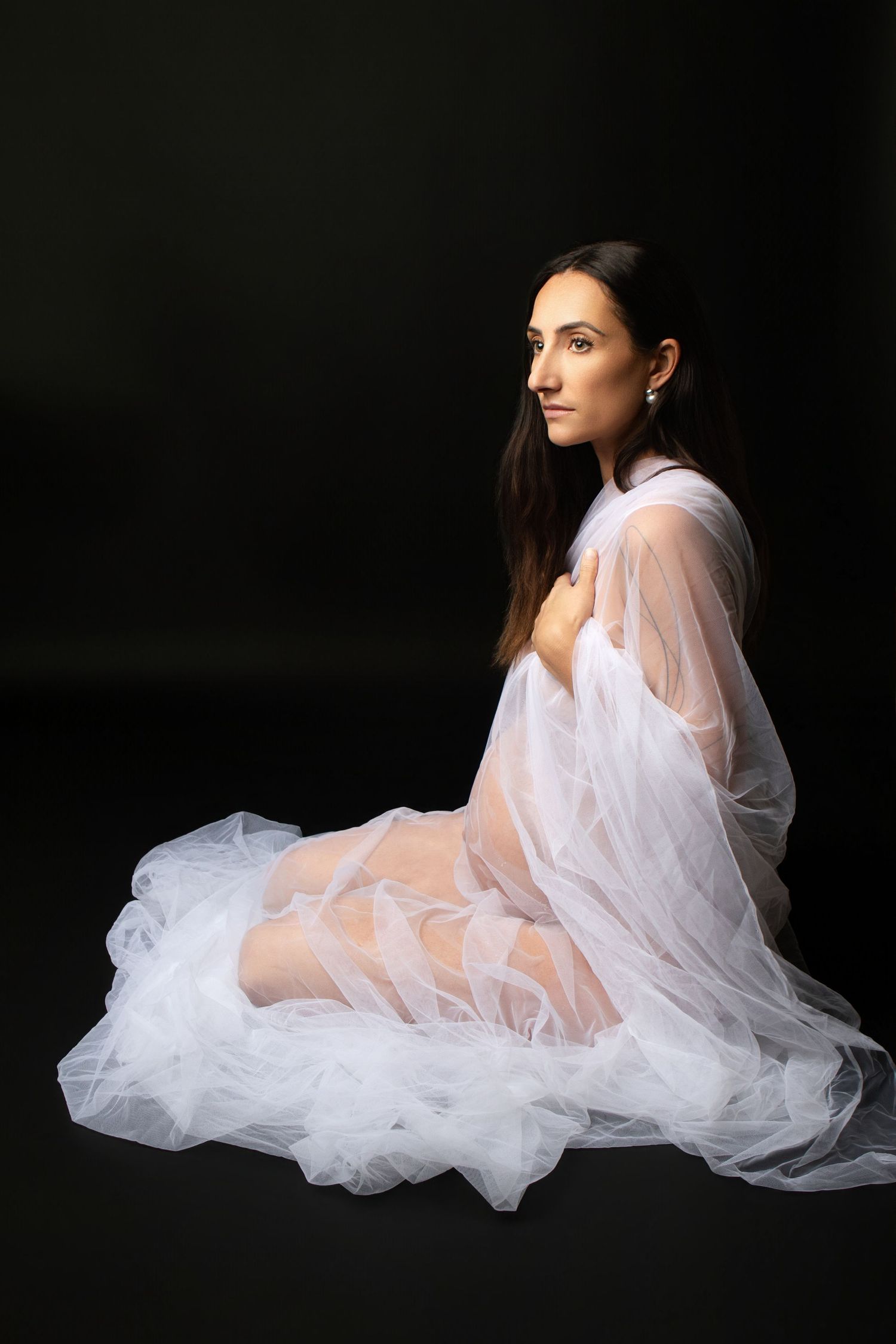 Pregnant woman in elegant red ruffled off-shoulder gown poses gracefully against black background.