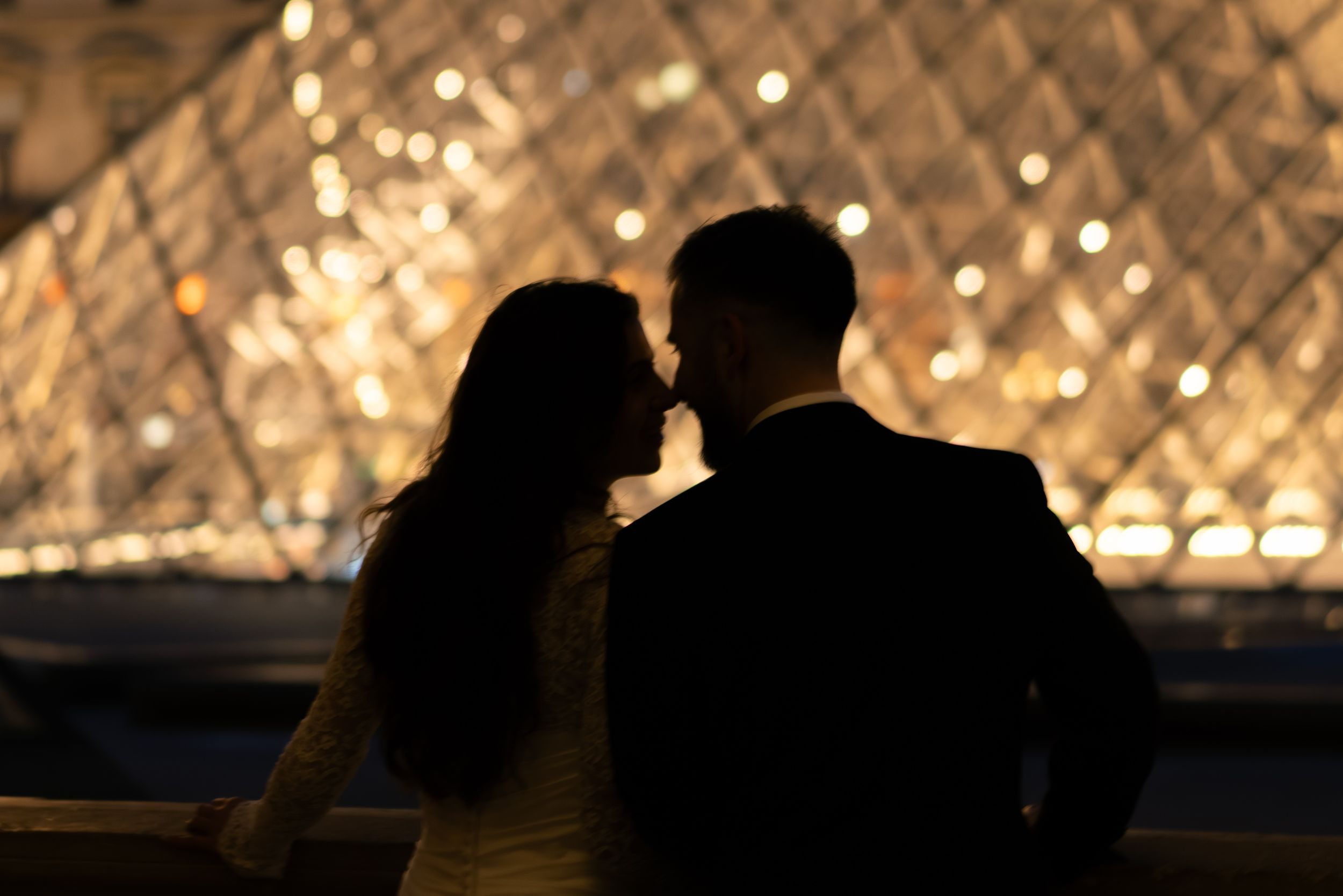Romantic couple silhouetted against the illuminated Louvre Pyramid in Paris at night. Couple kissing at the louvre at night. Silhouette