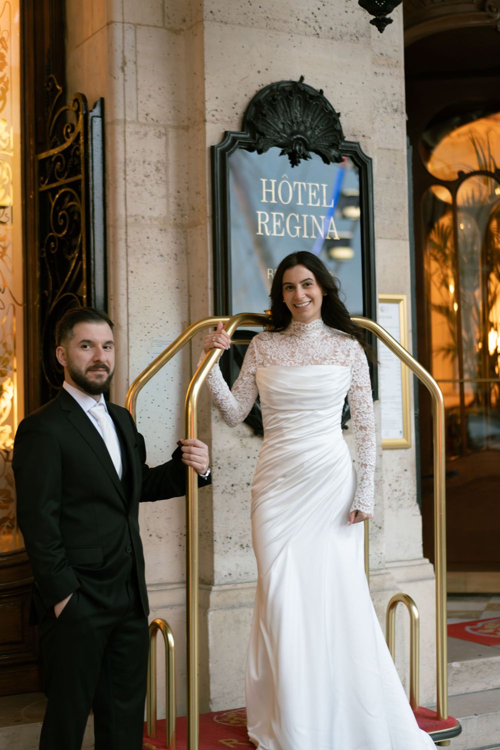 Bride and groom posing at the entrance of Hotel Regina Paris, bride in lace wedding gown, nighttime paris wedding photos, evening paris