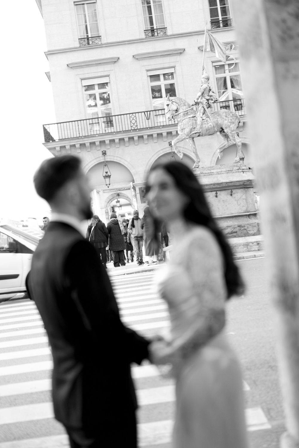 Black and white photo of an elegant couple holding hands near a Parisian building. CInematic paris wedding photography, film photography