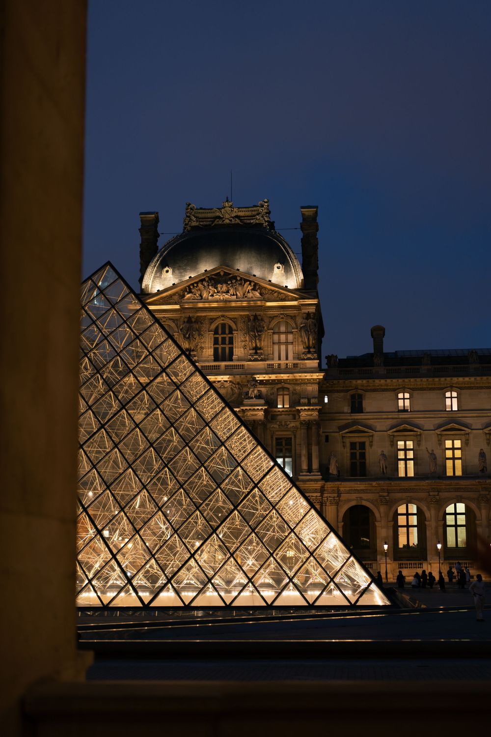 The illuminated glass Louvre Pyramid glows at night with the historic museum building behind it in Paris. Best paris wedding photographer.