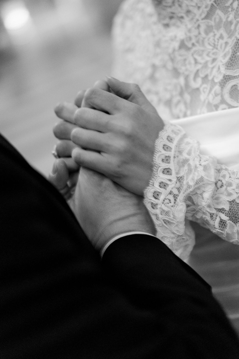 Close-up black and white photo of bride and groom holding hands, bride wearing lace sleeve wedding dress. Paris nighttime wedding
