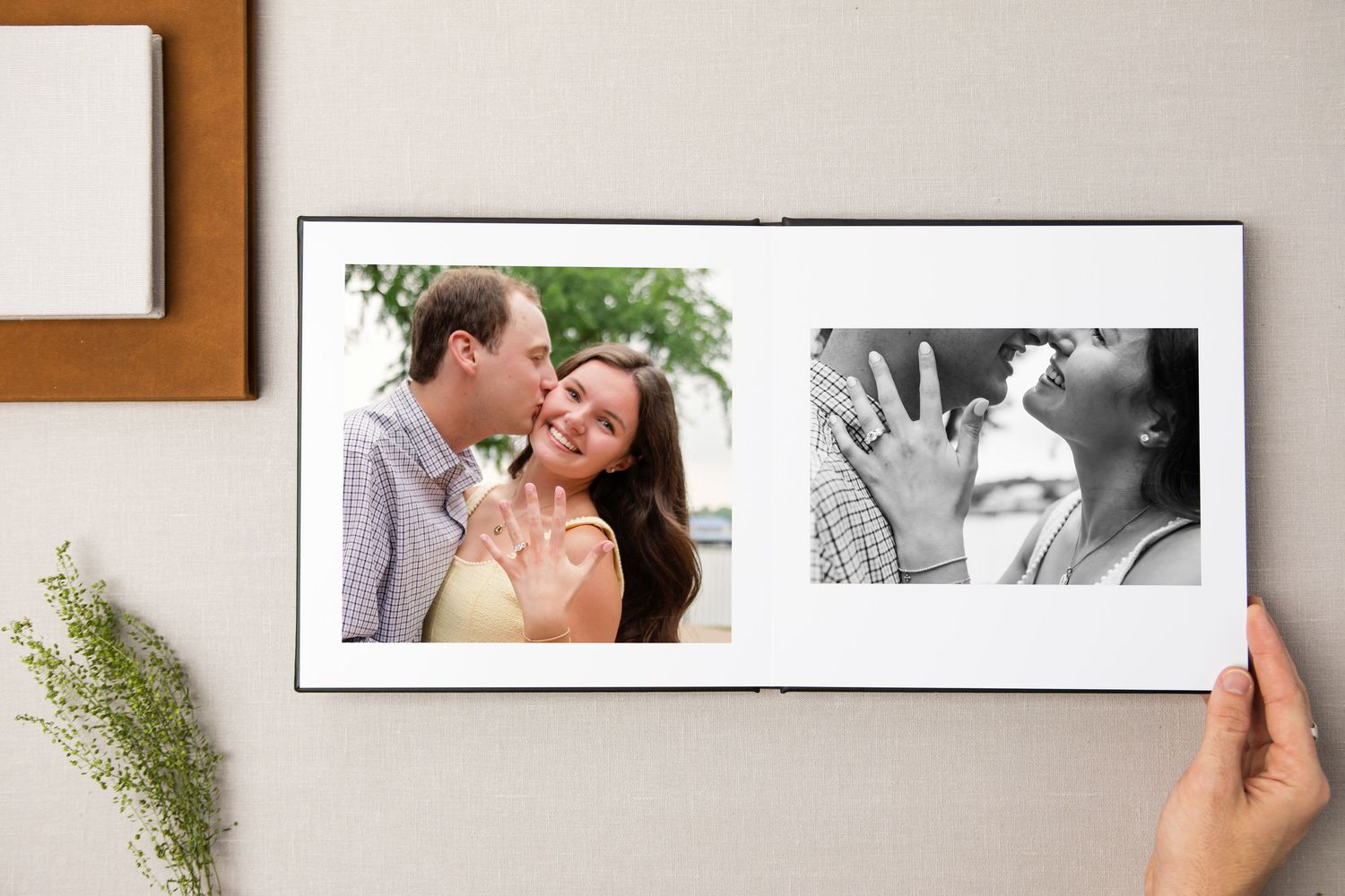 A hand holds open a photo book featuring a couple sharing a romantic moment and a black-and-white engagement ring photo in Keller, TX.