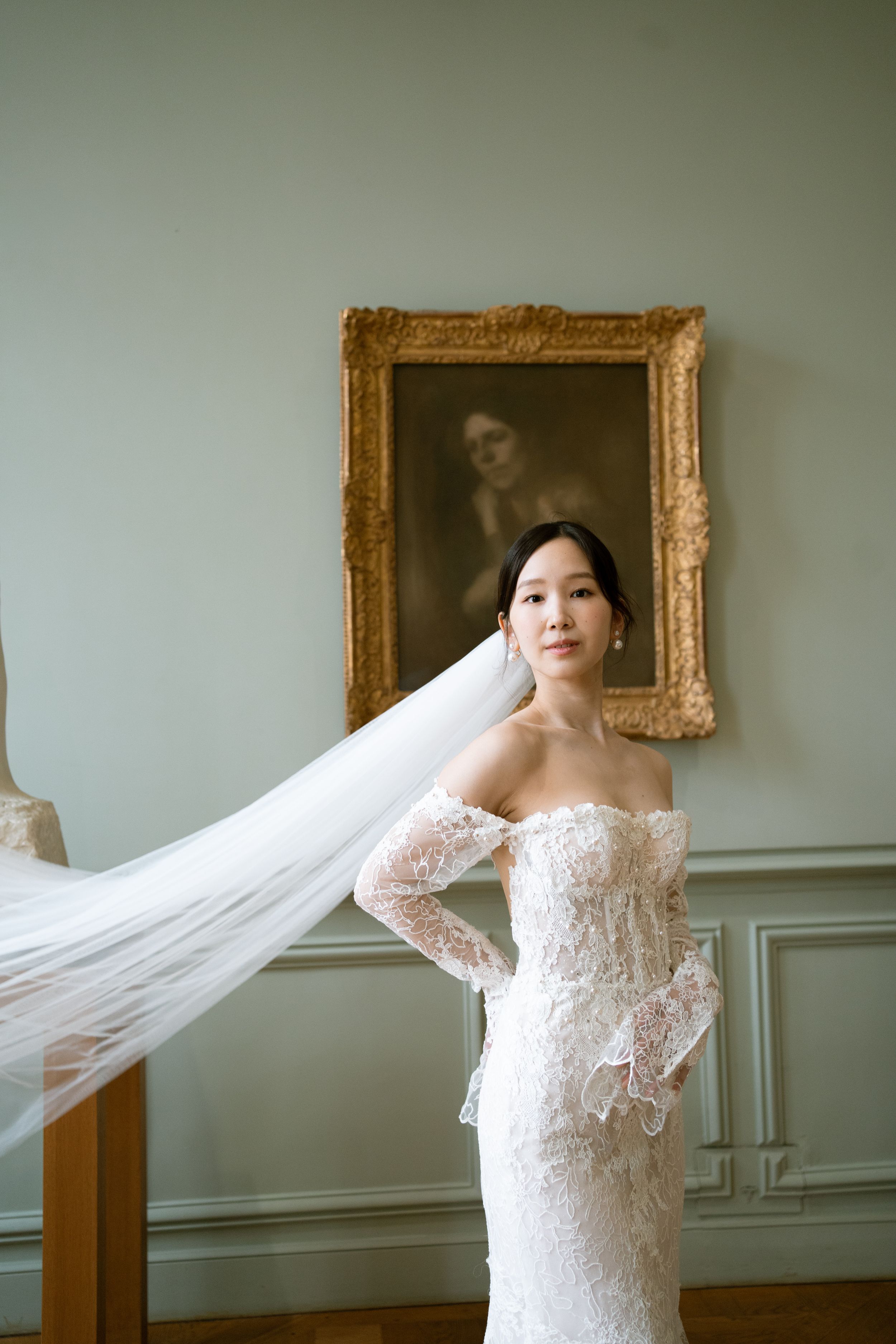 Bride in off-shoulder lace wedding gown with flowing veil billowing. Paris bride in museum. Paris bridal outfits. musee rodin wedding photos