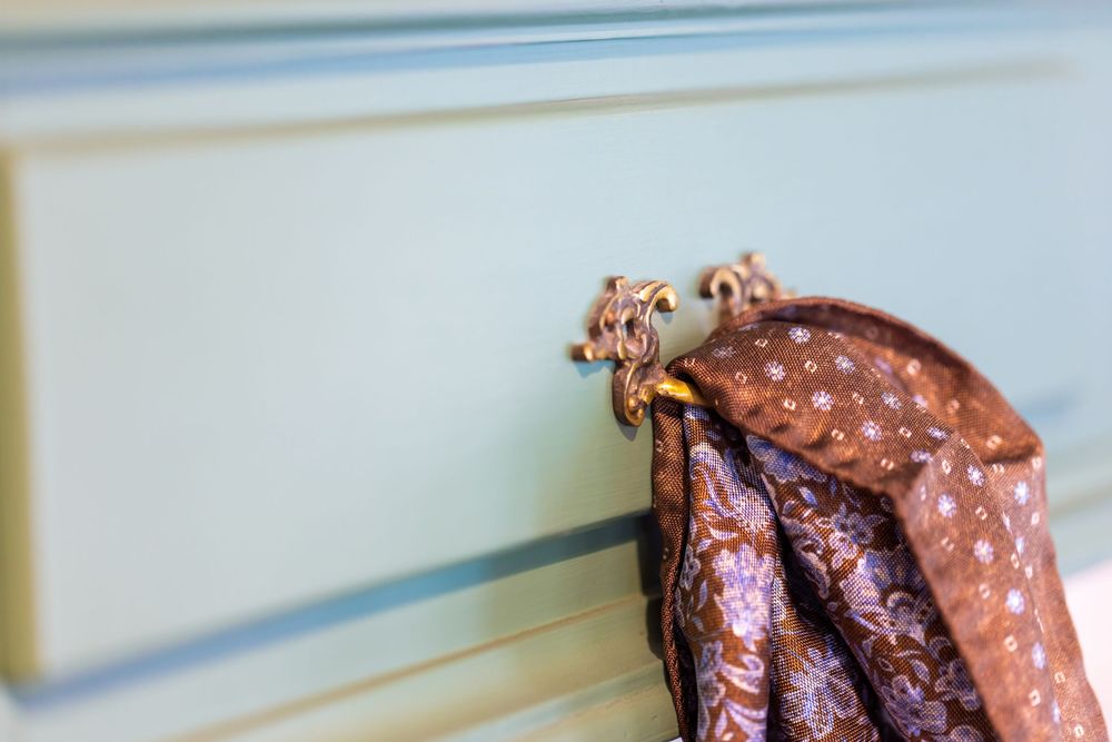 Ornate bronze hook on a light blue wall holding a brown floral scarf.