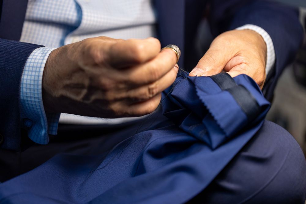 Close-up of hands adjusting a navy blue suit jacket lapel, showcasing fine tailoring and luxury fabric detail.