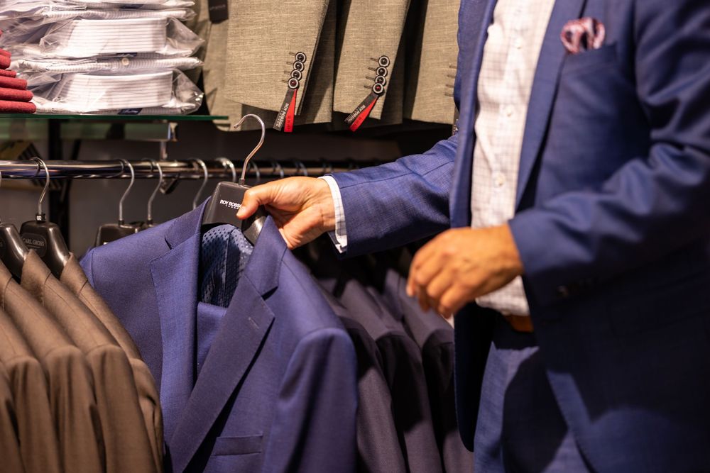 Man in blue suit browsing suits on a rack in a clothing store.