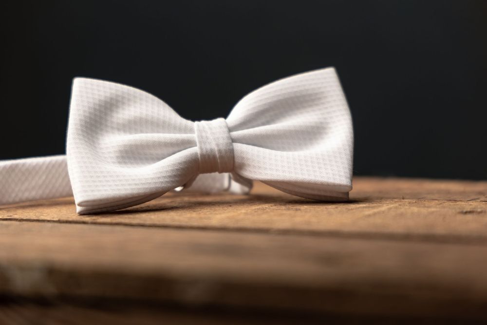 White bow tie resting on a rustic wooden surface against a dark background, perfect for formal occasions.