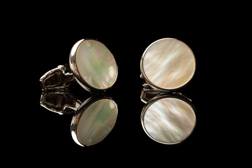 Round mother-of-pearl silver cufflinks with iridescent sheen displayed on black reflective surface.