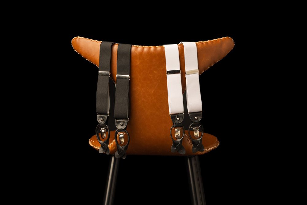 Brown leather bar stool with black metal legs, featuring black and white suspenders draped over the back.