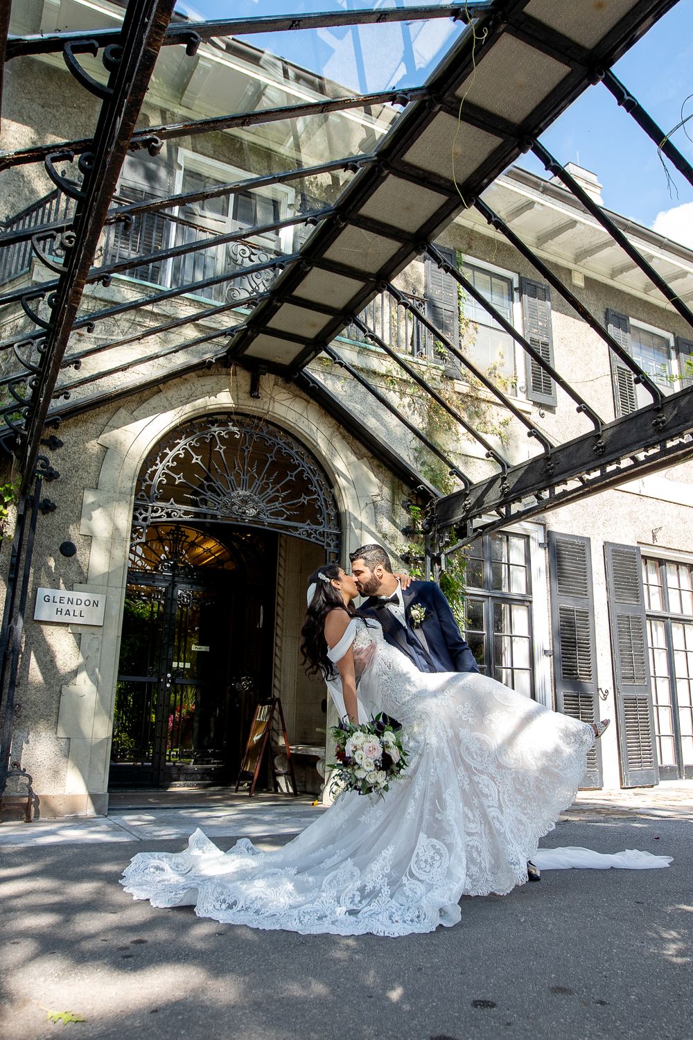 Groom dips bride in stunning lace wedding dress for a romantic kiss outside Glendon Hall.