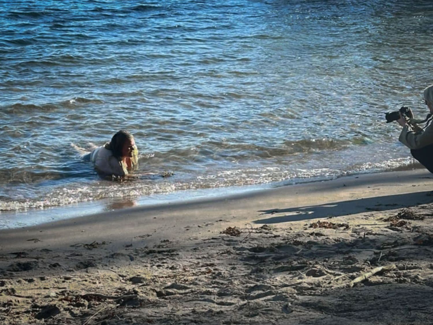 Behind the scenes när Fotograf Jessica Lindqvist fotograferar en kvinna som ligger i vattnet vid strandkanten.