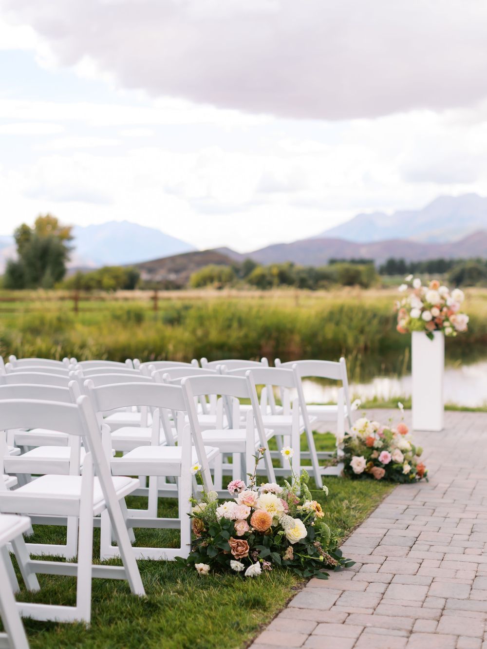 Outdoor wedding ceremony setup with white folding chairs, floral arrangements, and mountain views in the background.