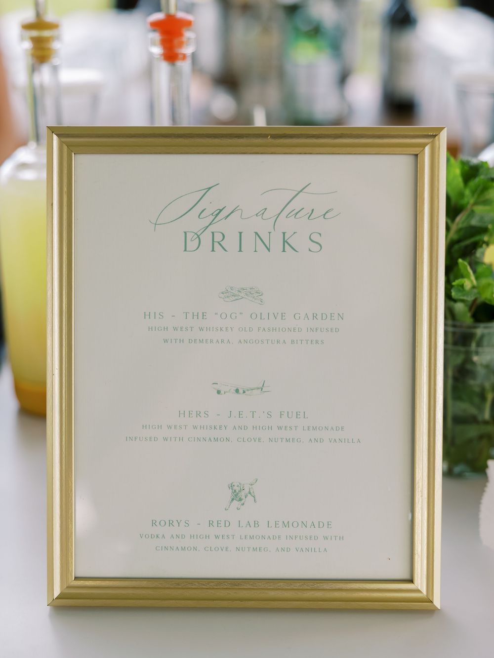 Elegant gold-framed signature drinks menu displayed at a wedding bar featuring his, hers, and pet-named cocktails.
