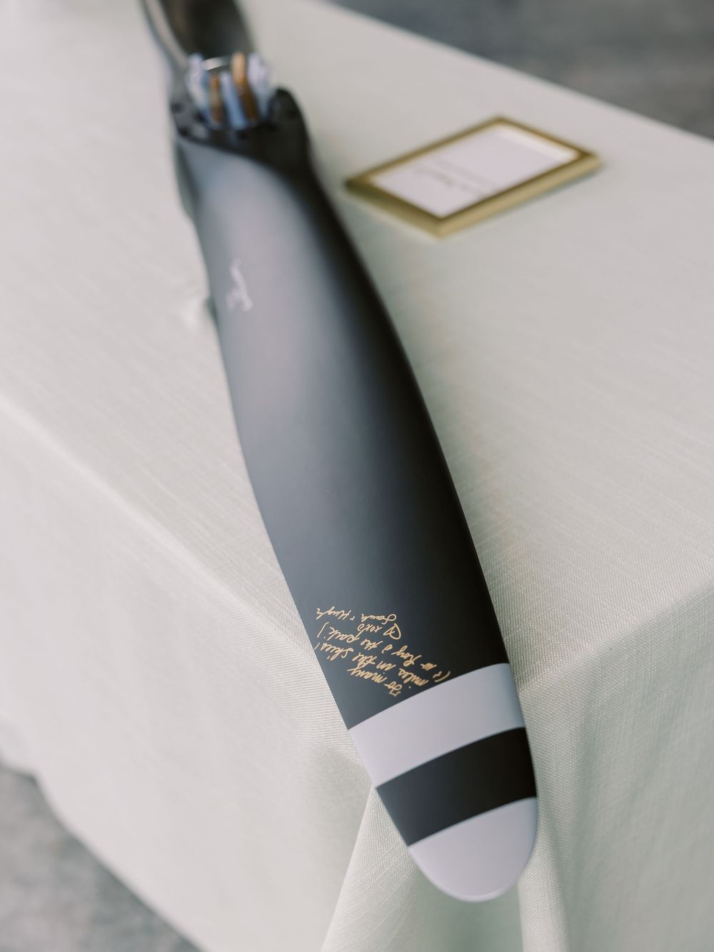 Black matte umbrella with gold script calligraphy and white stripe detail resting on a white linen table.