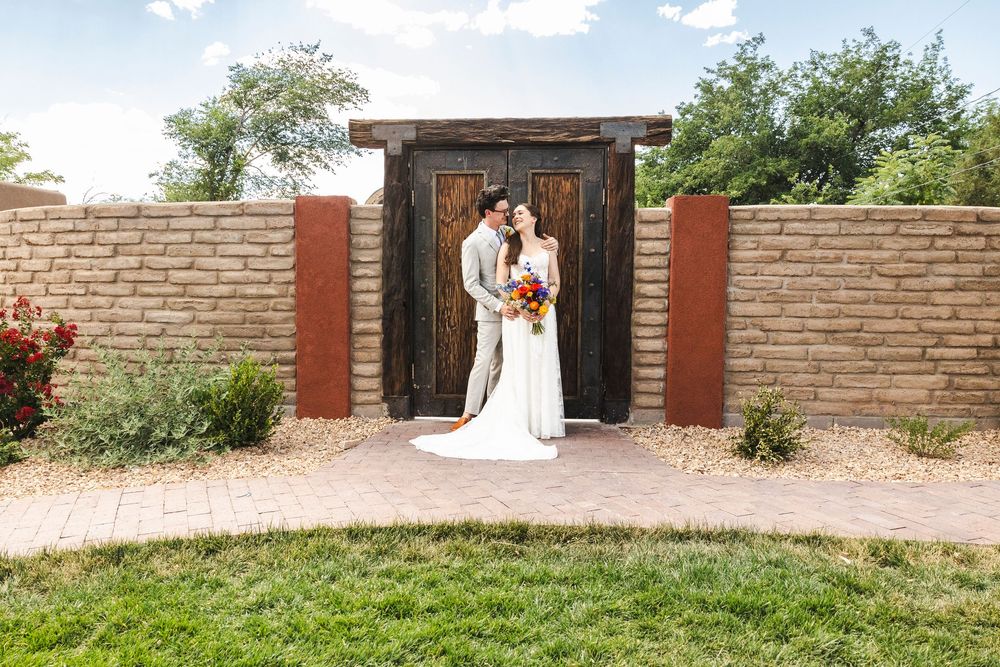 Bride and groom embracing in front of rustic wooden doors set in a adobe stone wall at an outdoor wedding venue.