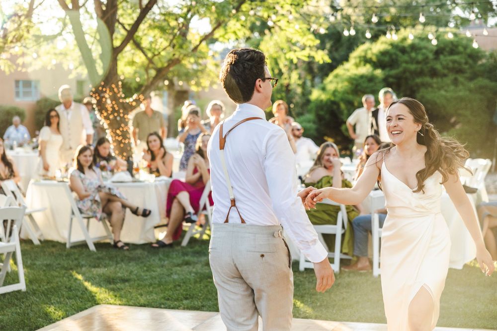 Bride and groom share first dance at outdoor wedding reception with guests seated at white tables.